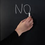 Close-up of a hand writing 'NO' on a chalkboard using white chalk.